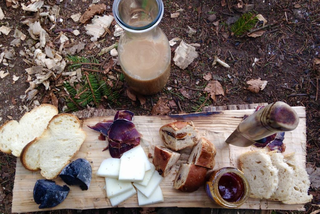 Auf einem Holzbrett liegen Zopfscheiben, Käste, getrocknetes Fleisch und Marmeladengläser.